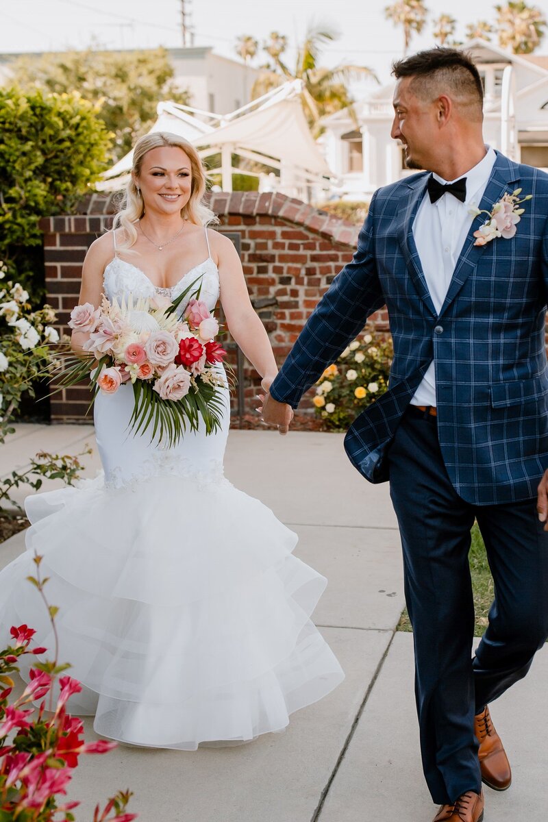 bride and groom hold hands as they walk, smiling