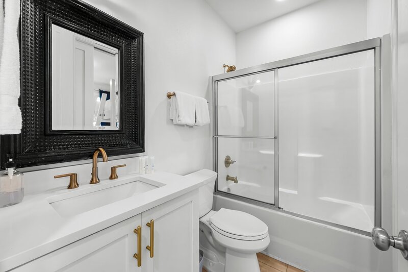 Modern bathroom with white vanity, gold hardware, and tub/shower combo—clean and stylish for relaxing beach stays in Panama City Beach.