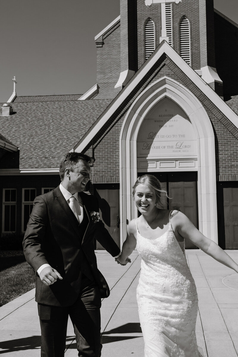 A newlywed couple holding hands and walking outside a church