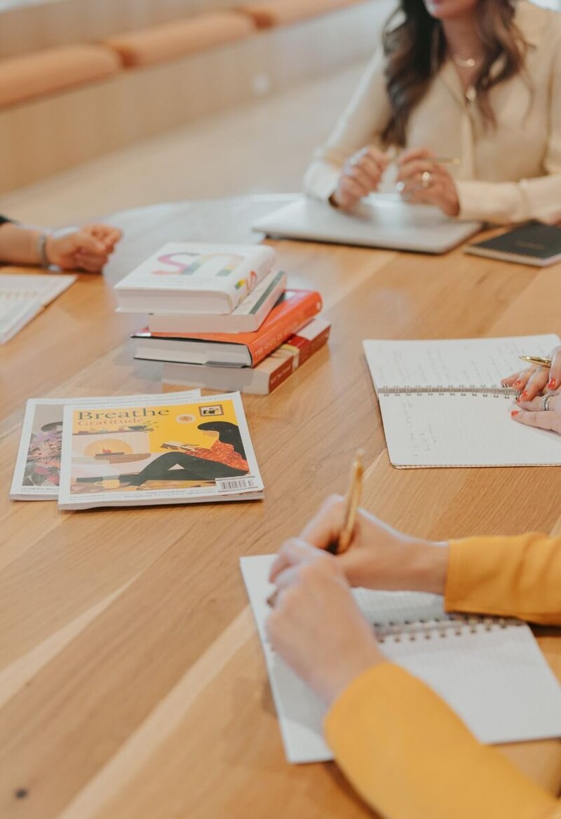 A desk with books and women sitting around. This is a formal clinical staff meeting at Relationship Experts office in Miami, florida. The team is discussing how to help more couples in the aftermath of infidelity heal, rebuild trust, and save their relationship.