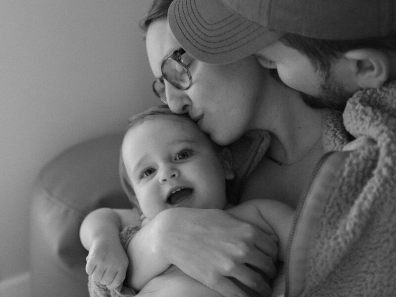 Black and white photo of Britni Dean and her husband kissing their daughter