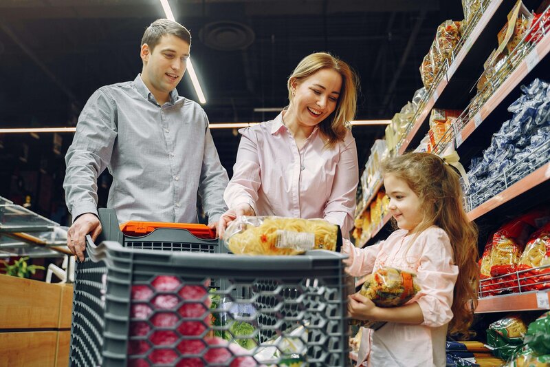 parents pushing a grocery cart smiling at daughter putting bread in the cart