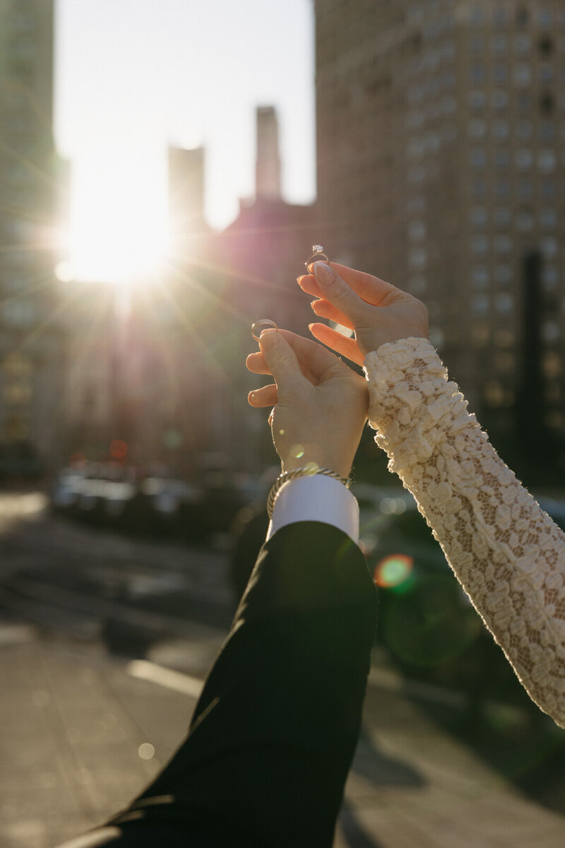 Bride and Groom holding their wedding bands in the sunset coming through the skyscrapers in New York City, NY, created by Andrea-Marie Photography
