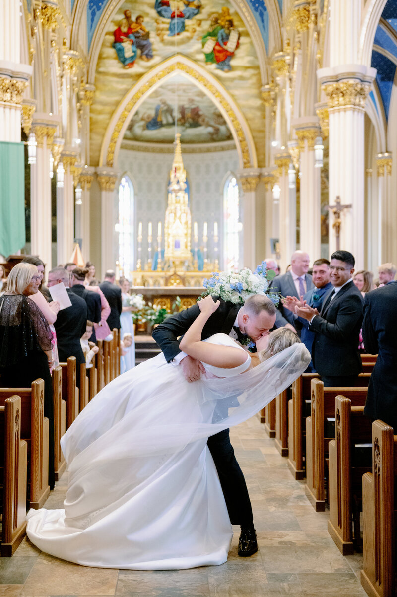 groom giving his bride a kiss while dipping her in the aisle of a church