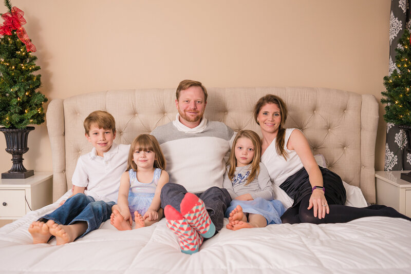 Christmas themed Family Portrait taken on a cream colored bed.  Photo taken by Dripping Springs Texas based Lydia Teague Photography.