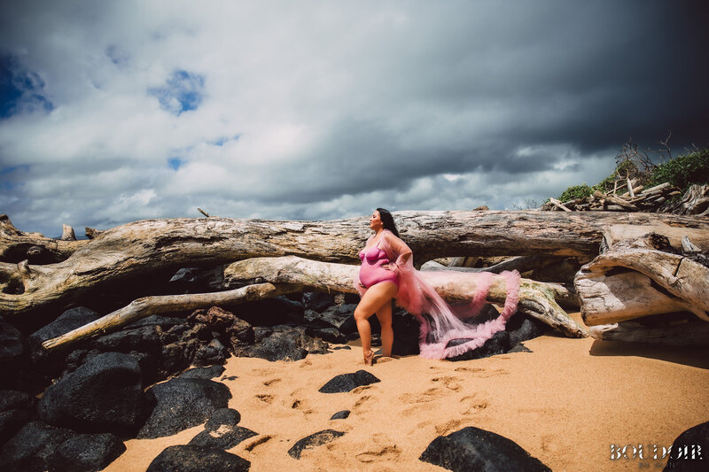 Beautfiul pregnant woman stands on Hawaii beach wearing luxury pink robe and lingerie