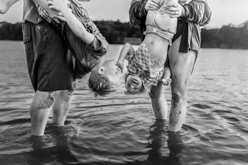 Mom and dad hold children upside down as they play in the lake during family session at photoshoot with Olathe KS photographer.