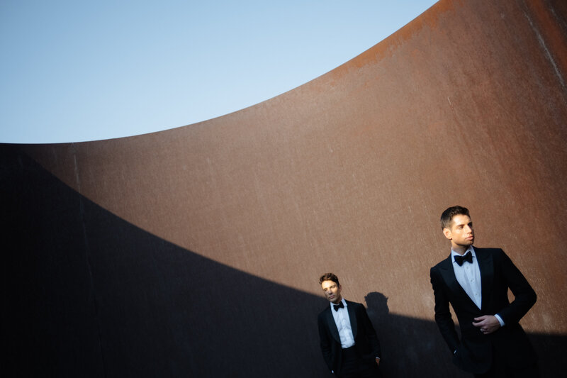 Groomsmen in tuxedos pose against dramatic modern architectural backdrop