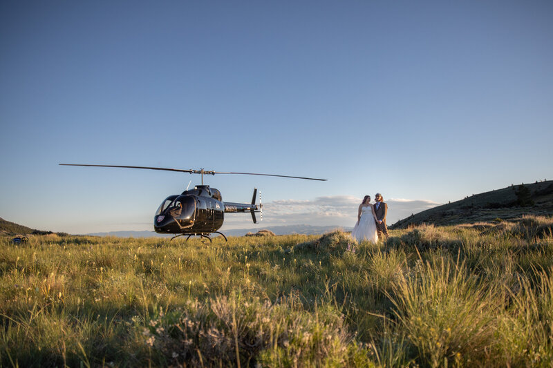 Bride and Groom stand in a meadow next to a elopement helicopter.