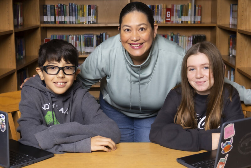 Microsoft Reading Coach teacher leaning between two students sitting at desk in library