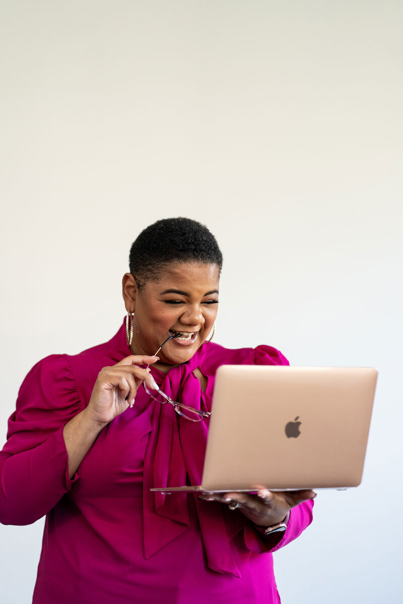 Career coaching for mid-level professionals, featuring a coach working on her laptop with clients. She wears a pink elegant blouse and holds reading glasses, exuding professionalism.