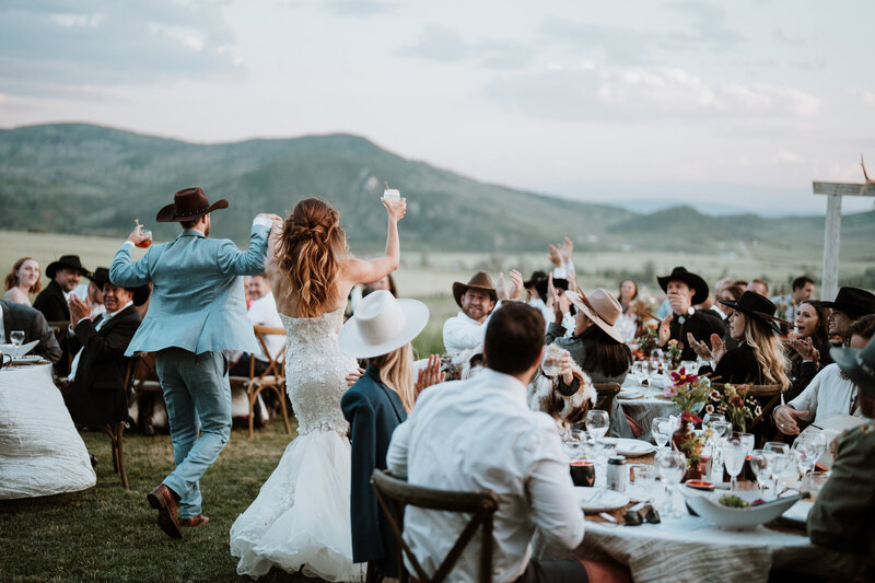 Bride and groom enter outdoor wedding reception in cowboy hats near Breckenridge, Colorado.