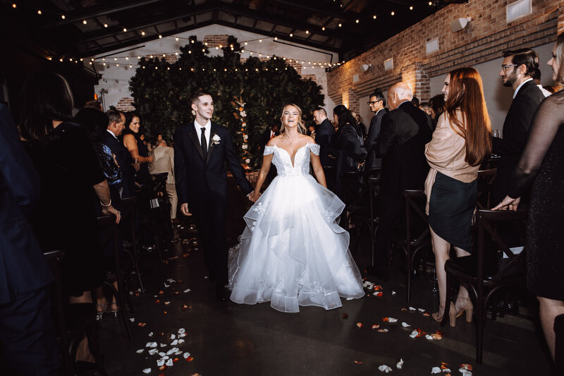 A bride and groom walk down the aisle together after their wedding ceremony smiling and laughing