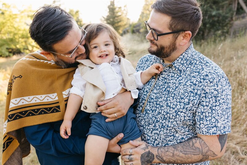 two dads snuggling their toddler son while playing in a field in healdsburg