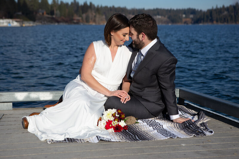 Bride and Groom on dock sharing a picnic and leaning together sitting down on a blanket