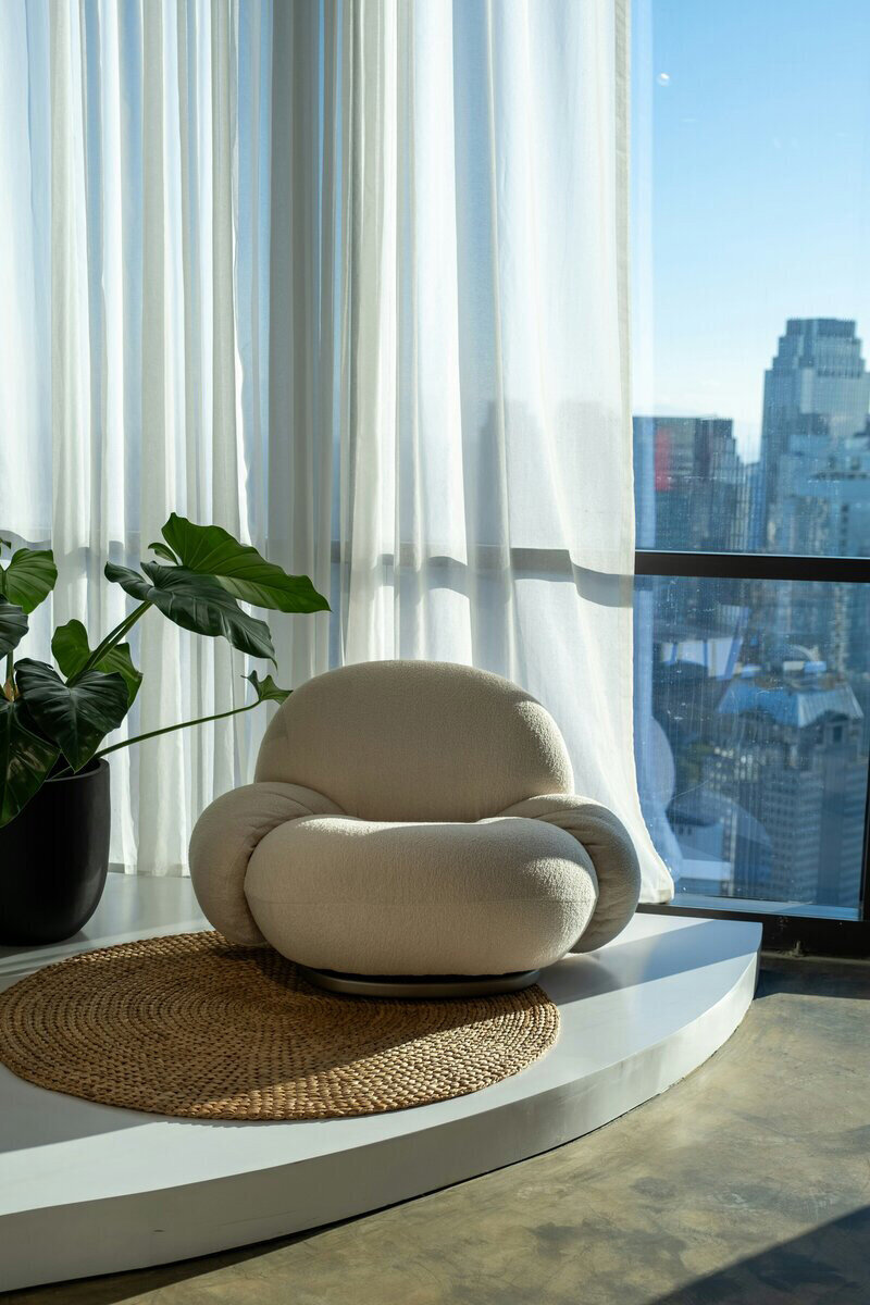 A cozy chair and a green plant sit by a bright window, creating a warm and inviting atmosphere.