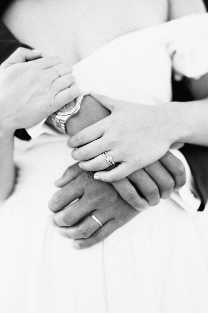 A film detail of the bride and groom holding hands with their wedding rings on. The black and white photo is shot on film by Megan Lynn of My Sun and Stars Co.