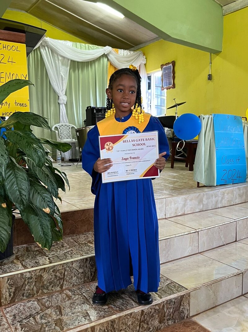 Little girl in blue graduation gown holding diploma for graduating pre-k in rural Jamaica