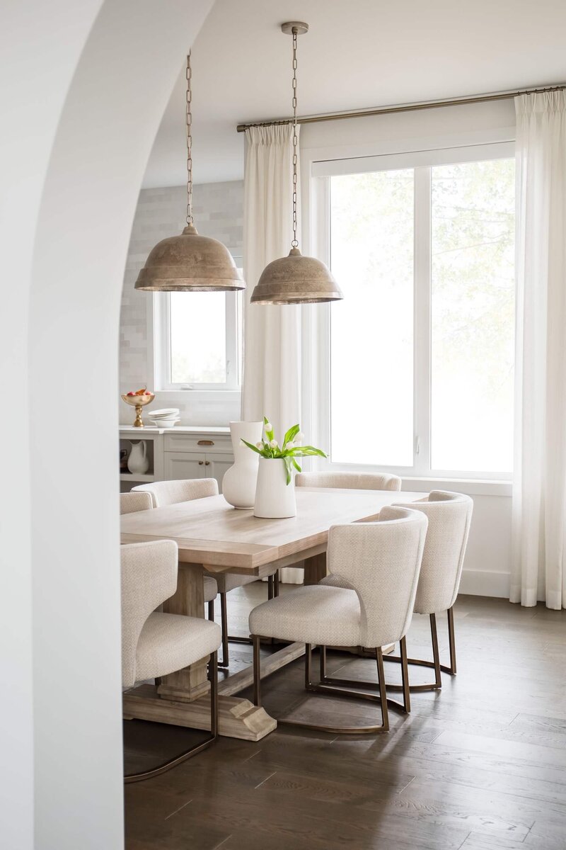 Wooden dining table with light upholstery and pendant lighting. 