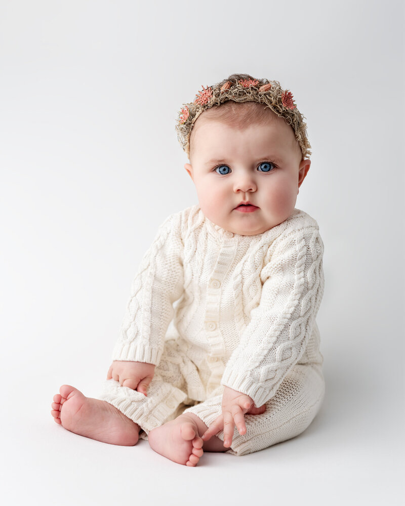 This elegant milestone portrait features a baby girl styled in soft neutrals, surrounded by timeless textures and gentle light.