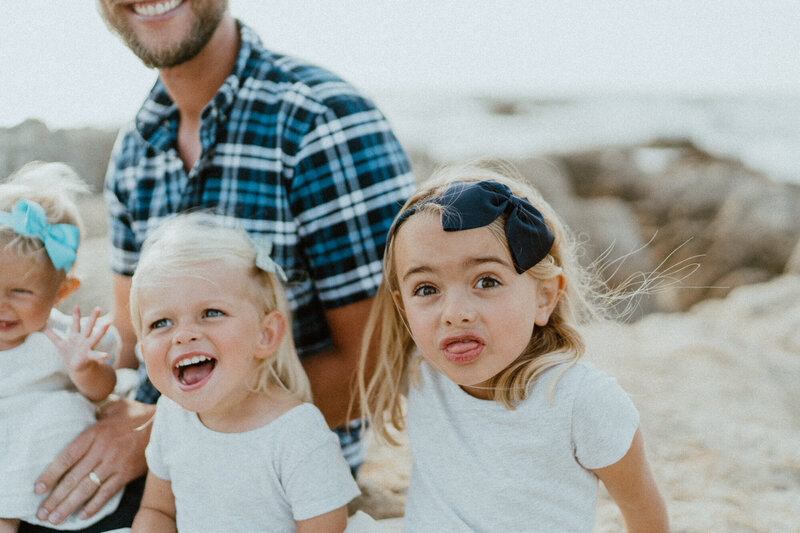 young sisters making silly faces on beach with dad