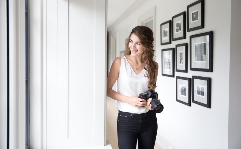 NY Branding Photographer Laura Volpacchio poses for photo smiling while holding camera.