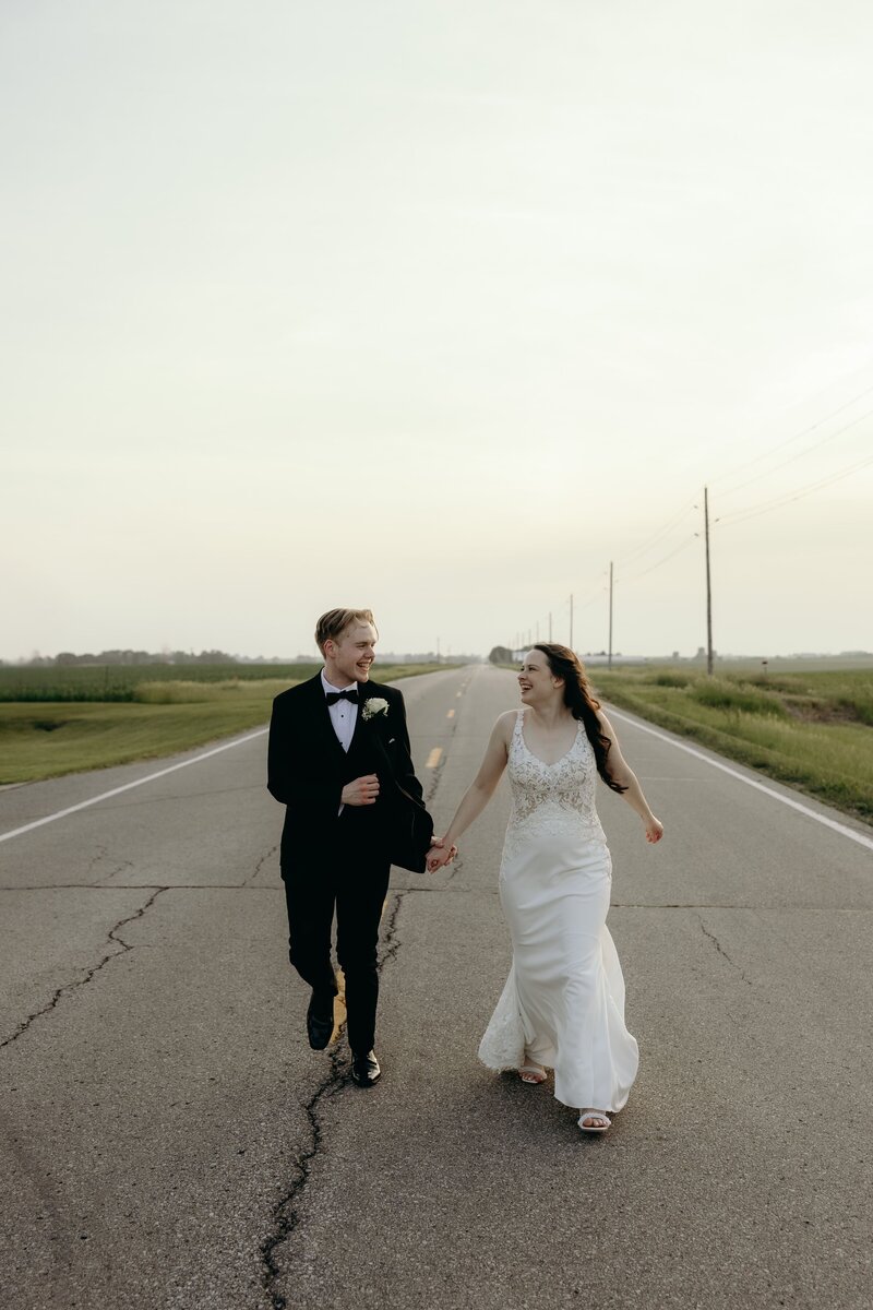 Joy-filled newlyweds run hand in hand down a road in eastern Iowa.
