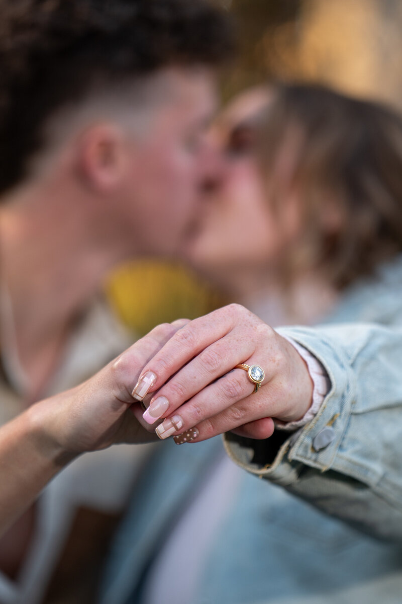 A couple kissing while holding out a hand showing off an engagement ring 