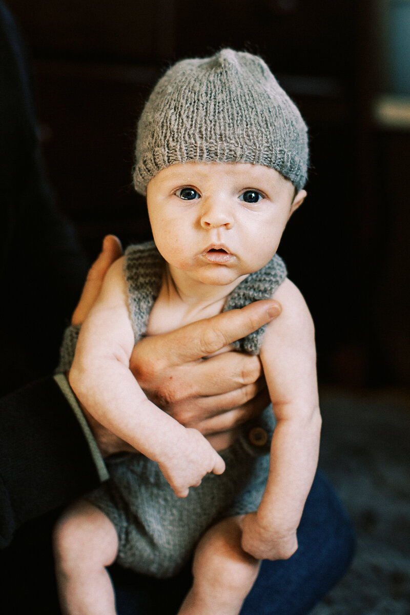 baby boy in knit hat and overalls stares at camera
