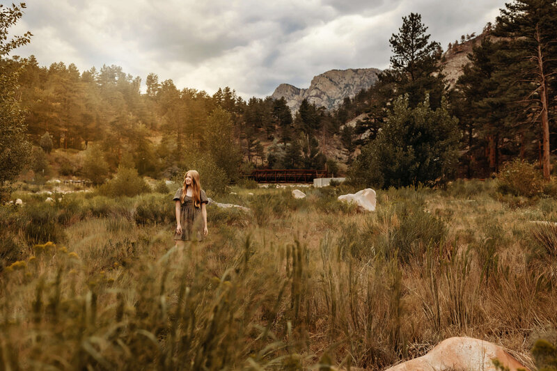 High school senior walking in  a field at sunset with Rocky Mountains behind her.