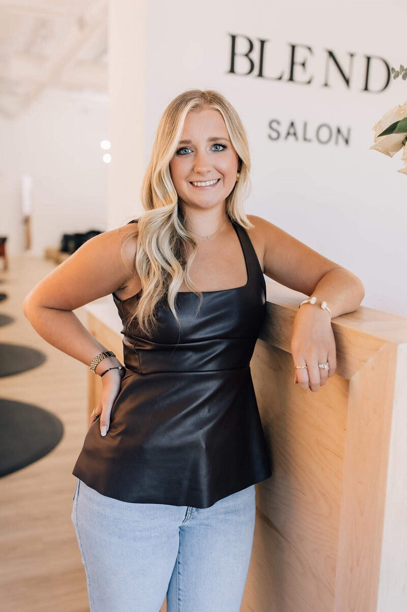 Headshot of certified hair stylist with blond hair extensions smiling wearing black