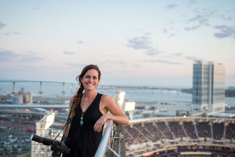 A portrait of Bernadette and her camera with the Coronado Bridge and stadium behind her