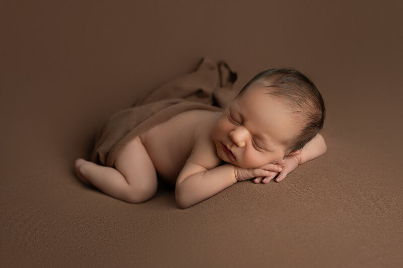 Newborn photography session in Austin Texas featuring baby in natural pose on brown backdrop