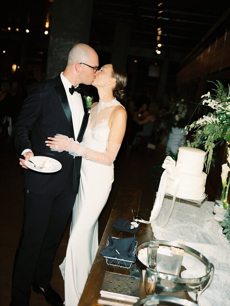 image by mimmesota wedding photographer tom thornton of bride and groom kissing near cake on wedding day while holding plate