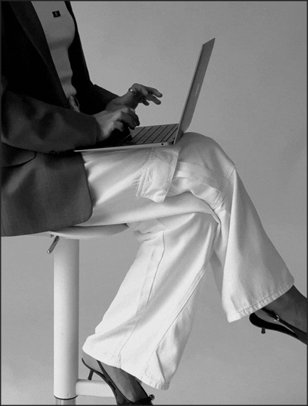 Woman typing on a laptop sitting on a stool