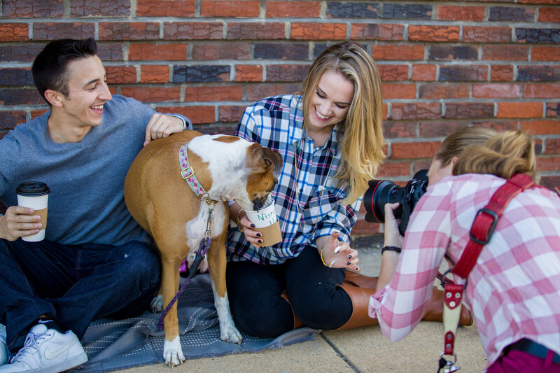 Jen Stitt capturing a playful moment of a dog drinking a pupachino during an engagement session, highlighting the couple’s love for their pet and adding a lighthearted touch to their photoshoot.