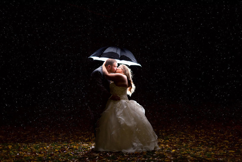 A kiss in the rain at night time under a lit umbrella