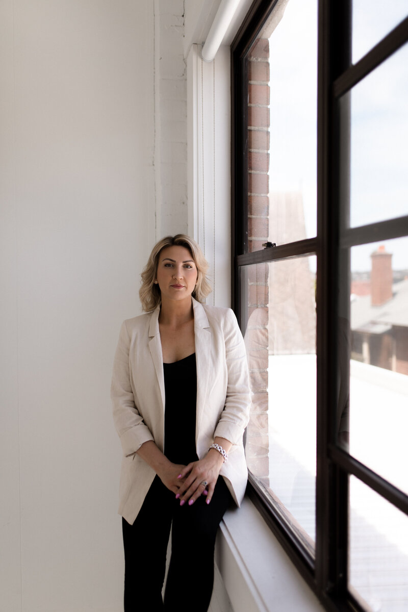 Lady with white blazer standing next to window