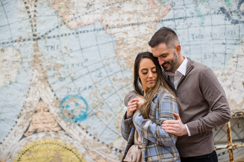 Engaged couple snuggled together in front of the Phoenixville Map mural, showcasing their connection and love for the town.