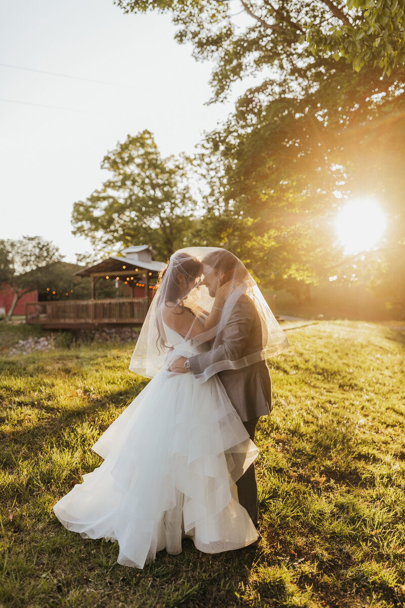 wedding couple embracing under veil with golden sun behind them
