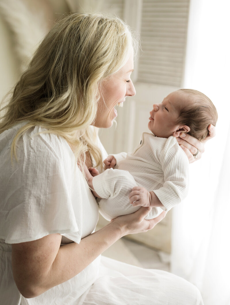mom in white dress holding newborn baby boy for studio newborn session cleveland family photographer