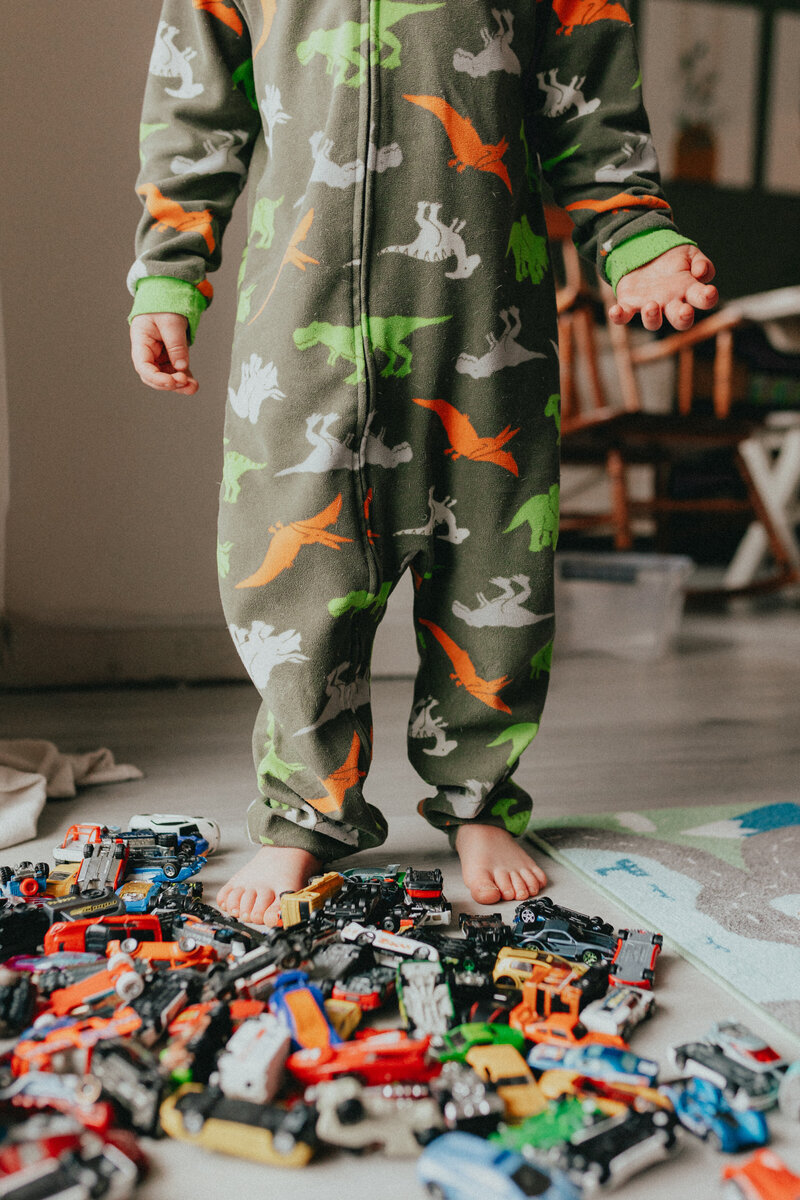 photo of a little boy taken from the shoulders down wearing pjs with his how wheels cars surrounding his bare feet taken by a langley newborn photographer