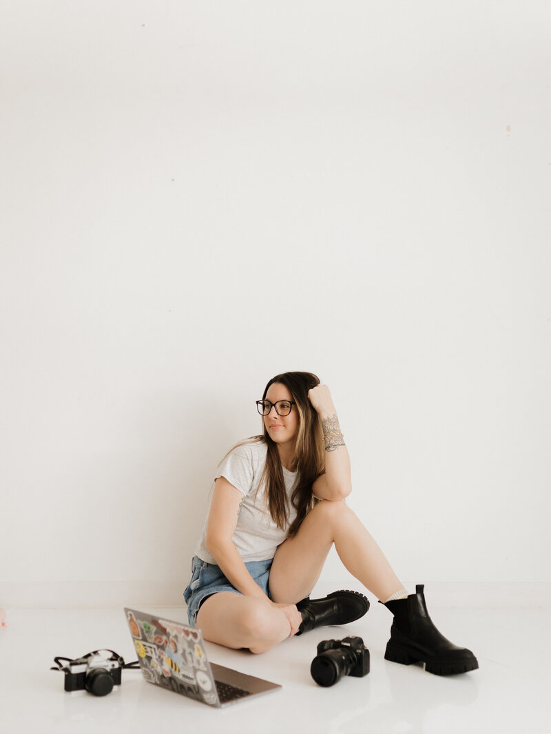 photo of a langley newborn photographer sitting on the ground with her gear around her on the floor and her head propped on her hands and smiling away from the camera