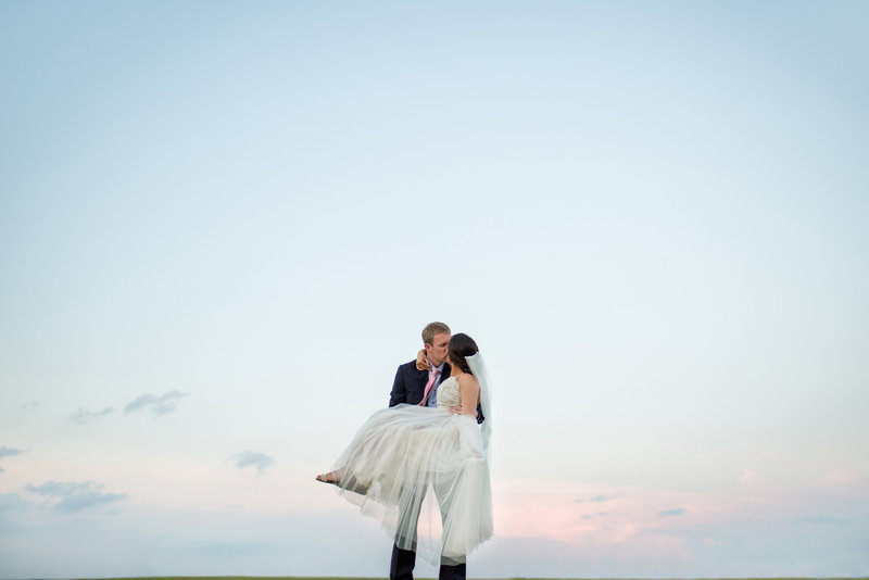 Groom kissing his bride during a summer sunset