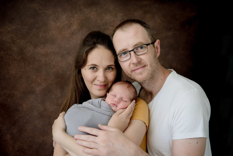 mom and dad holding their newborn baby boy who is wrapped in grey for their newborn photography session in Burlington, Ontario.
