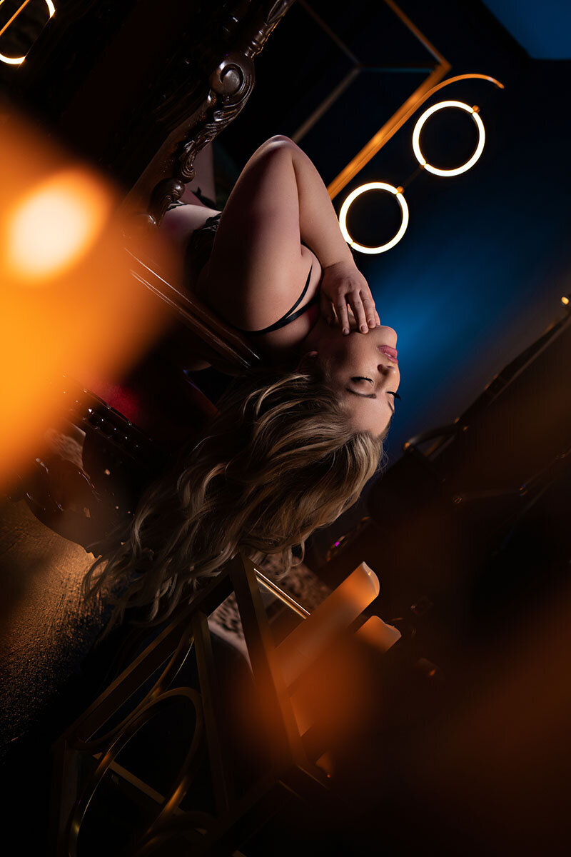 A woman with long hair reclines upside down on a red chair, surrounded by a warm glow. Circular lights in the background create a dreamy atmosphere.