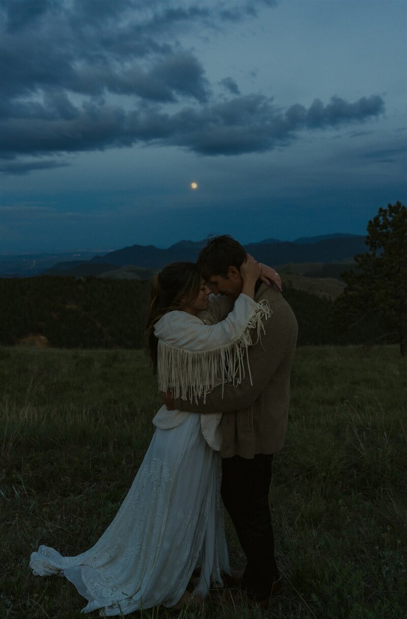 A bride and groom on a mountain overlook about to kiss.