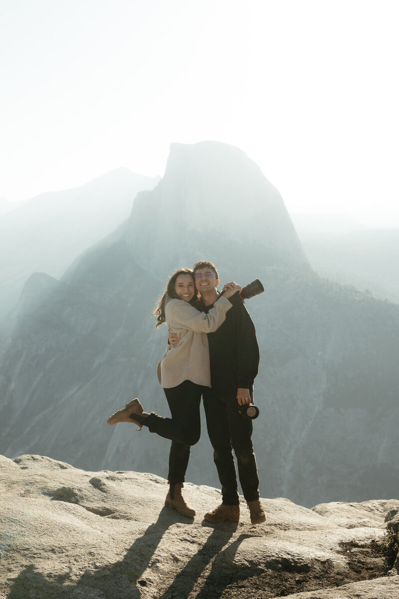 Yosemite Elopement Photographers The Chaffins standing in front of Glacier point smiling with cameras in their hands