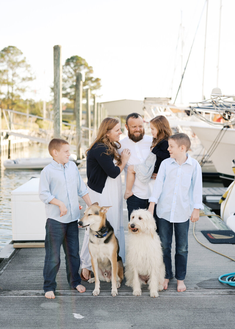 outdoor Virginia Beach Family Photography session on a dock where mom and dad are smiling and dogs are sitting with brother