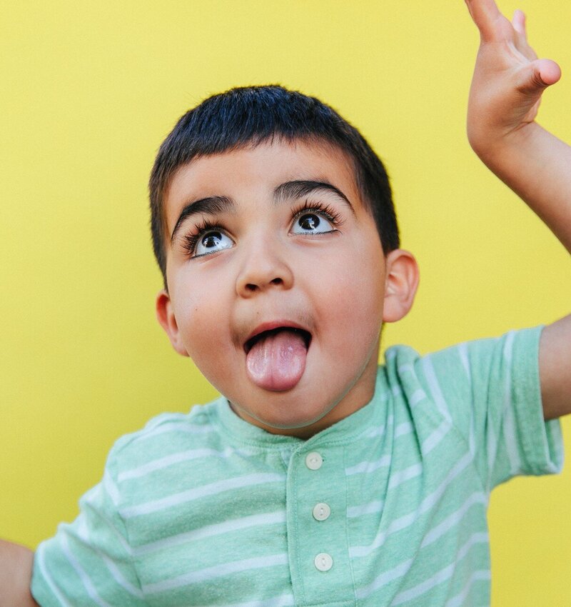 boy with long eyelashes making silly face with a bright yellow backdrop behind him